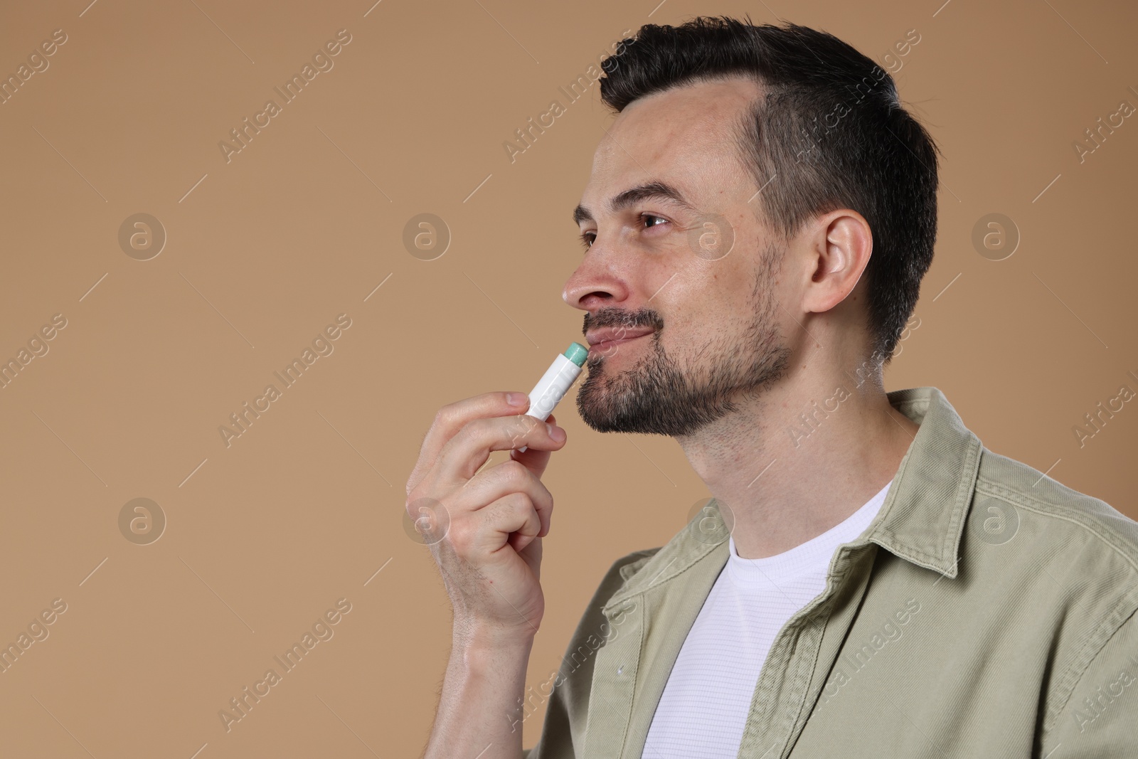 Handsome man applying lip balm onto his lips on light brown background. Space for text Photo of Handsome man applying lip balm onto his lips on light brown background. Space for text