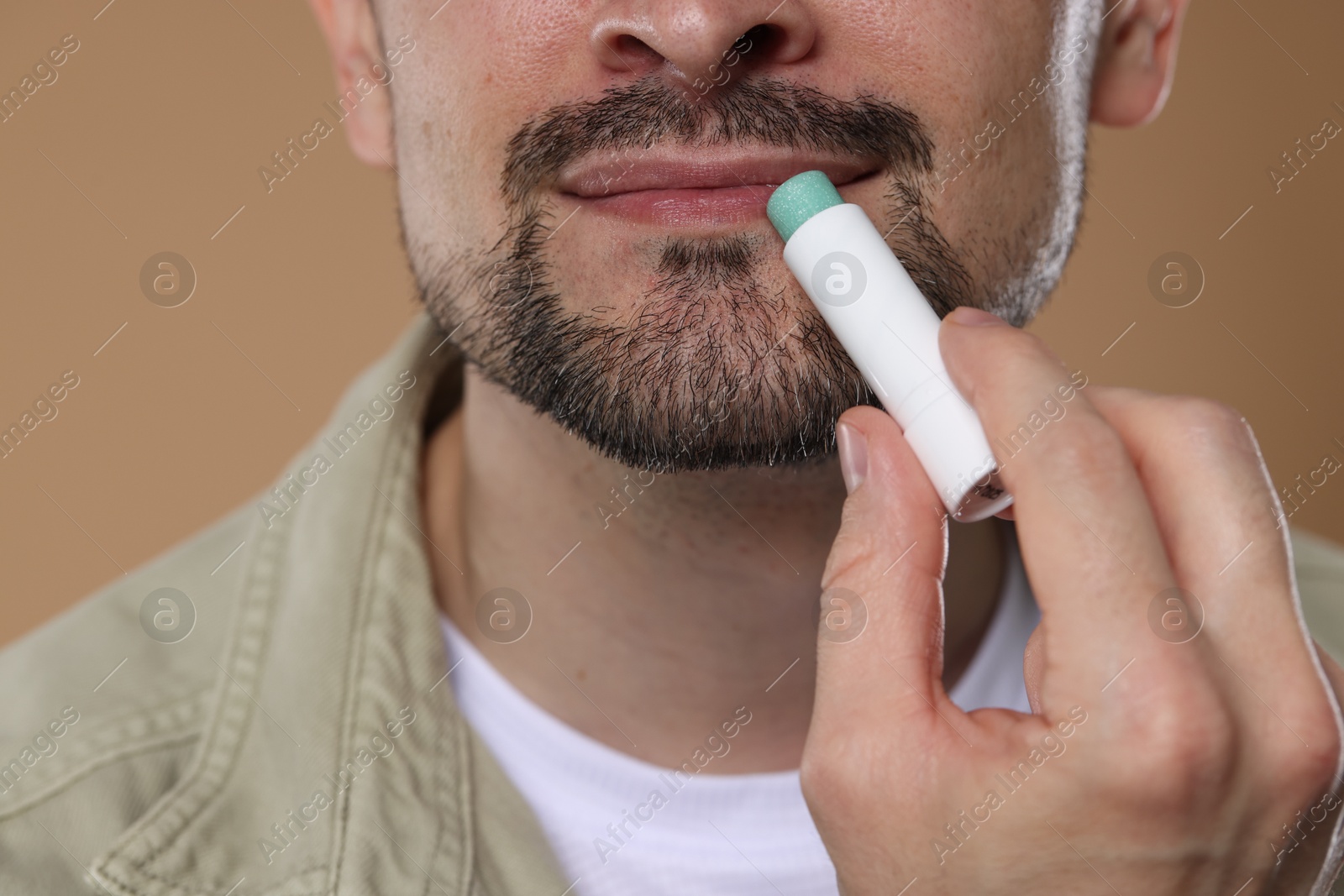 Man applying lip balm onto his lips on light brown background, closeup Photo of Man applying lip balm onto his lips on light brown background, closeup