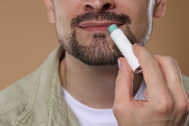 Photo of Man applying lip balm onto his lips on light brown background, closeup