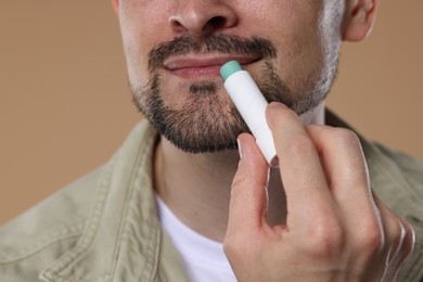 Photo of Man applying lip balm onto his lips on light brown background, closeup