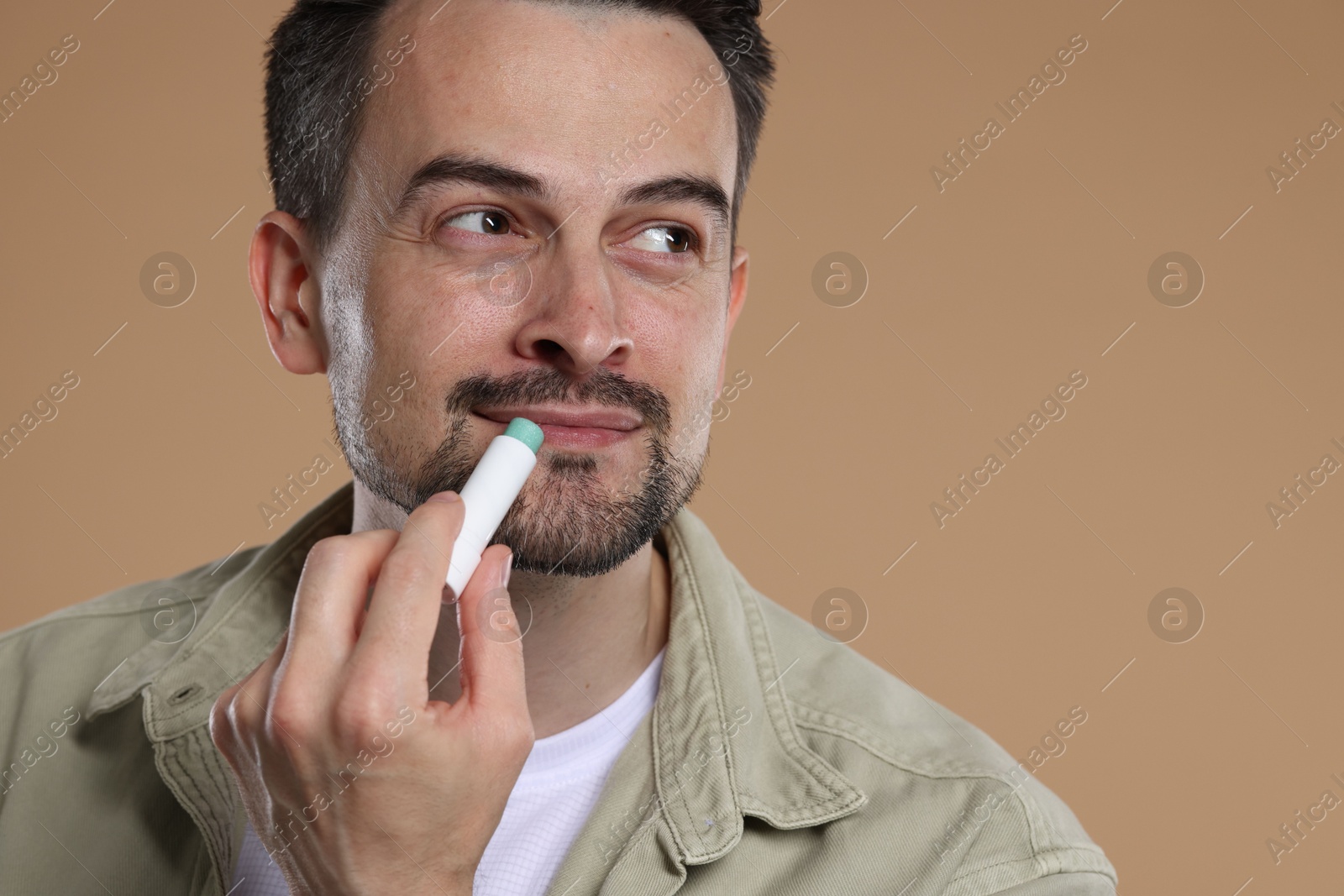 Handsome man applying lip balm onto his lips on light brown background Photo of Handsome man applying lip balm onto his lips on light brown background