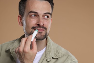 Photo of Handsome man applying lip balm onto his lips on light brown background