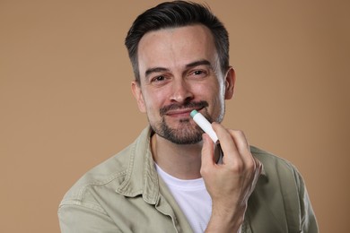 Photo of Handsome man applying lip balm onto his lips on light brown background