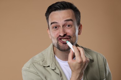 Photo of Funny man applying lip balm onto his lips on light brown background