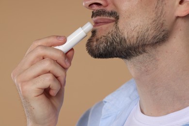Photo of Man applying lip balm onto his lips on light brown background, closeup