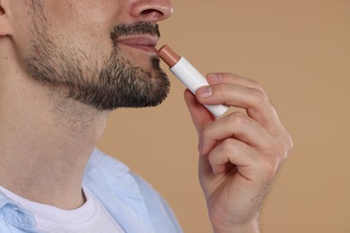 Photo of Man applying lip balm onto his lips on light brown background, closeup