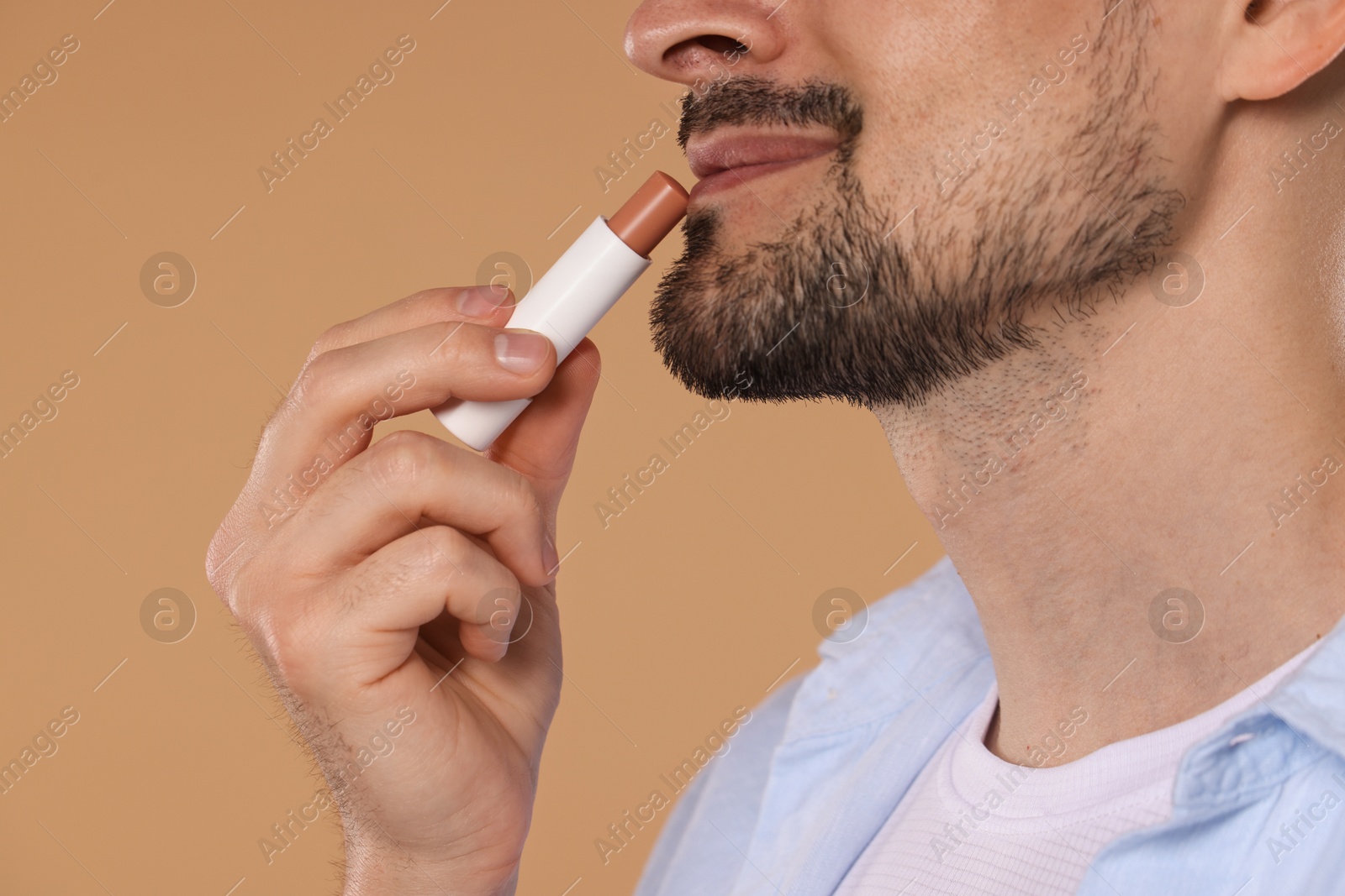 Man applying lip balm onto his lips on light brown background, closeup Photo of Man applying lip balm onto his lips on light brown background, closeup