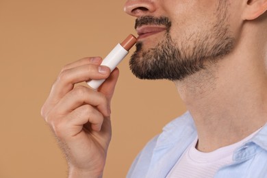 Photo of Man applying lip balm onto his lips on light brown background, closeup