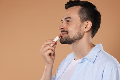 Photo of Handsome man applying lip balm onto his lips on light brown background. Space for text