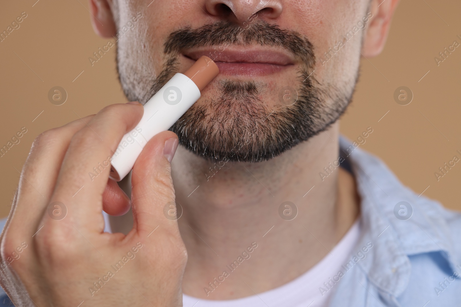 Man applying lip balm onto his lips on light brown background, closeup Photo of Man applying lip balm onto his lips on light brown background, closeup