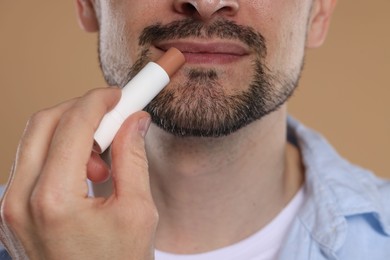 Photo of Man applying lip balm onto his lips on light brown background, closeup