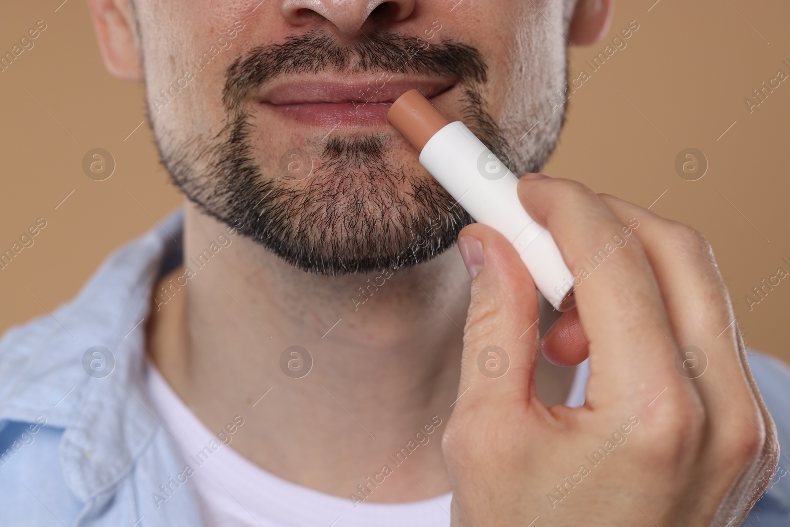 Man applying lip balm onto his lips on light brown background, closeup Photo of Man applying lip balm onto his lips on light brown background, closeup