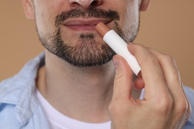 Photo of Man applying lip balm onto his lips on light brown background, closeup
