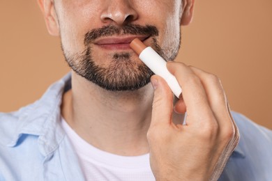 Photo of Man applying lip balm onto his lips on light brown background, closeup