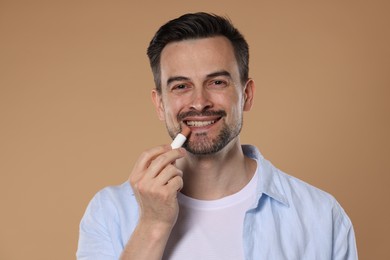 Photo of Smiling man applying lip balm onto his lips on light brown background