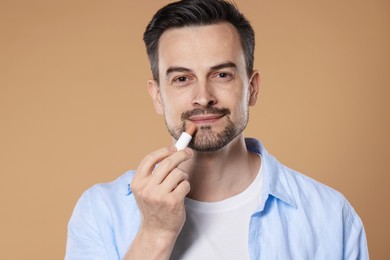 Photo of Handsome man applying lip balm onto his lips on light brown background