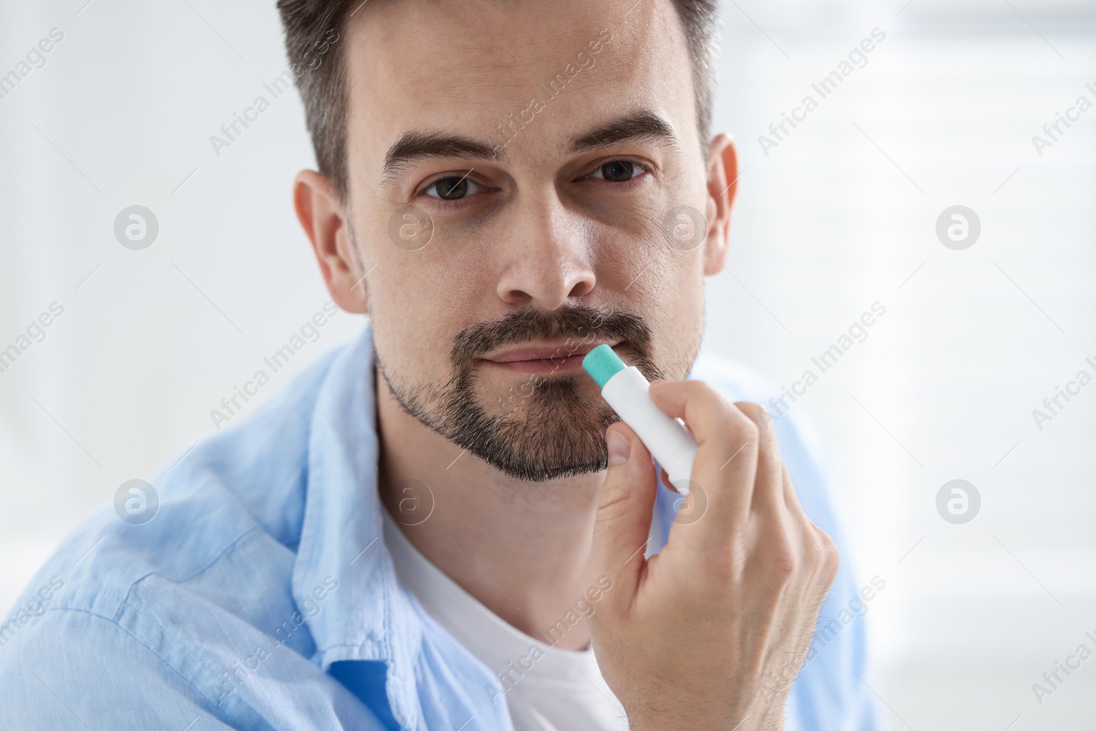 Handsome man applying lip balm onto his lips on blurred light background Photo of Handsome man applying lip balm onto his lips on blurred light background