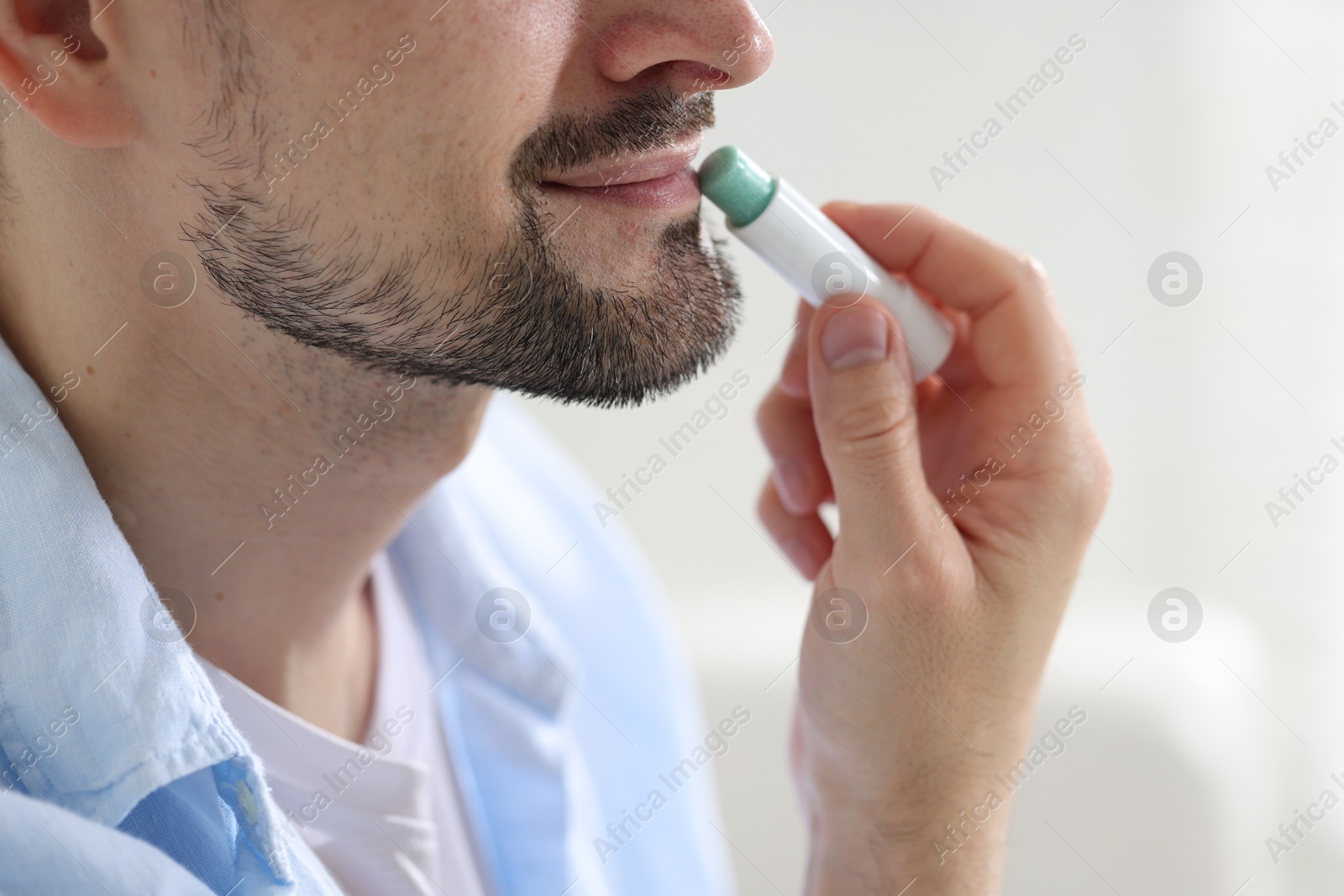 Man applying lip balm onto his lips on blurred light background, closeup Photo of Man applying lip balm onto his lips on blurred light background, closeup