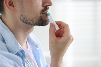 Photo of Man applying lip balm onto his lips on blurred light background, closeup