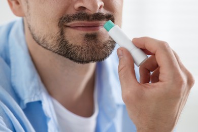 Photo of Man applying lip balm onto his lips on blurred light background, closeup