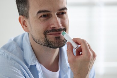 Photo of Handsome man applying lip balm onto his lips on blurred light background