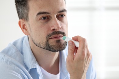 Photo of Handsome man applying lip balm onto his lips on blurred light background