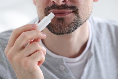 Photo of Man applying lip balm onto his lips on blurred light background, closeup