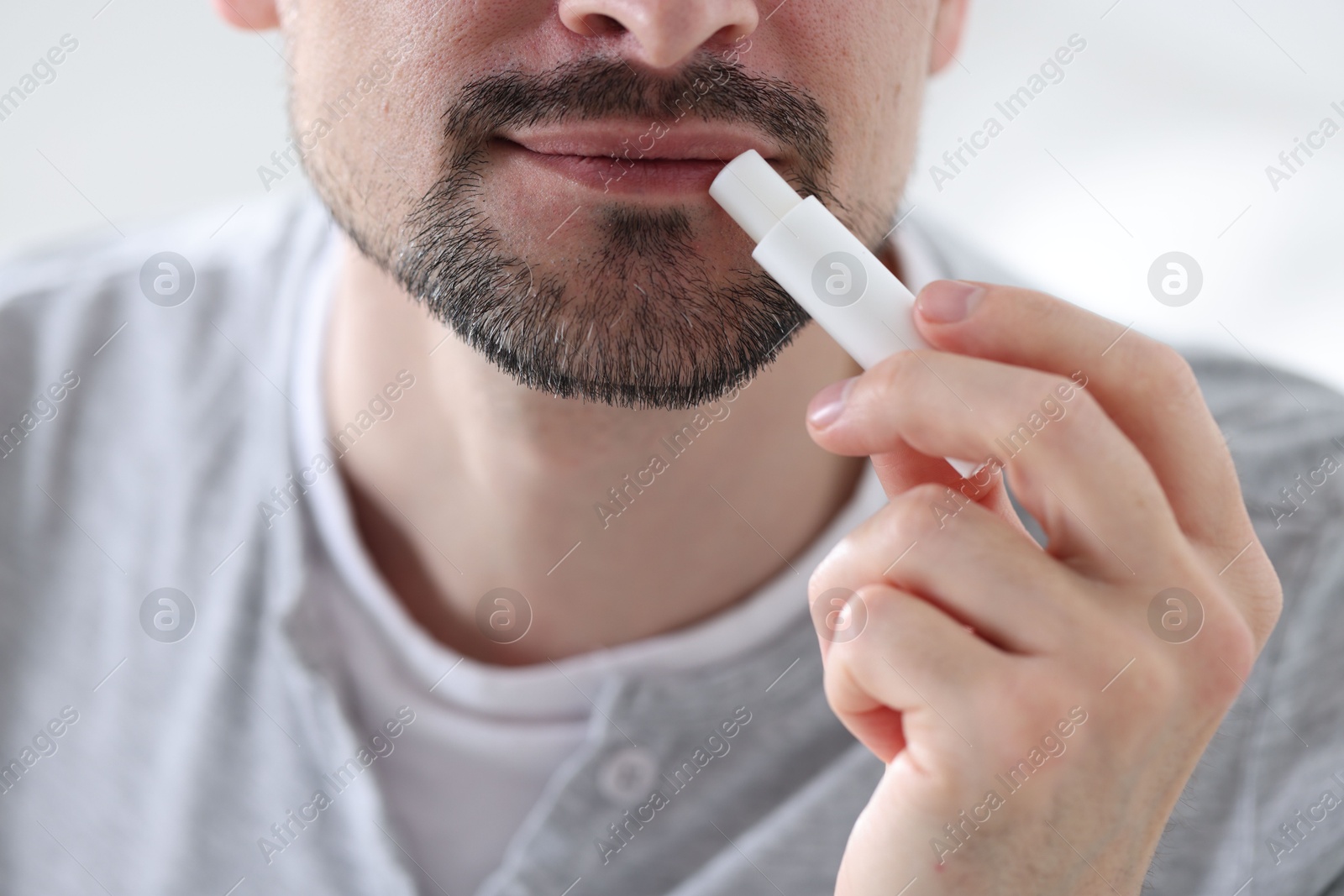 Man applying lip balm onto his lips on blurred light background, closeup Photo of Man applying lip balm onto his lips on blurred light background, closeup