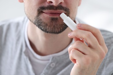 Photo of Man applying lip balm onto his lips on blurred light background, closeup
