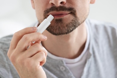 Photo of Man applying lip balm onto his lips on blurred light background, closeup