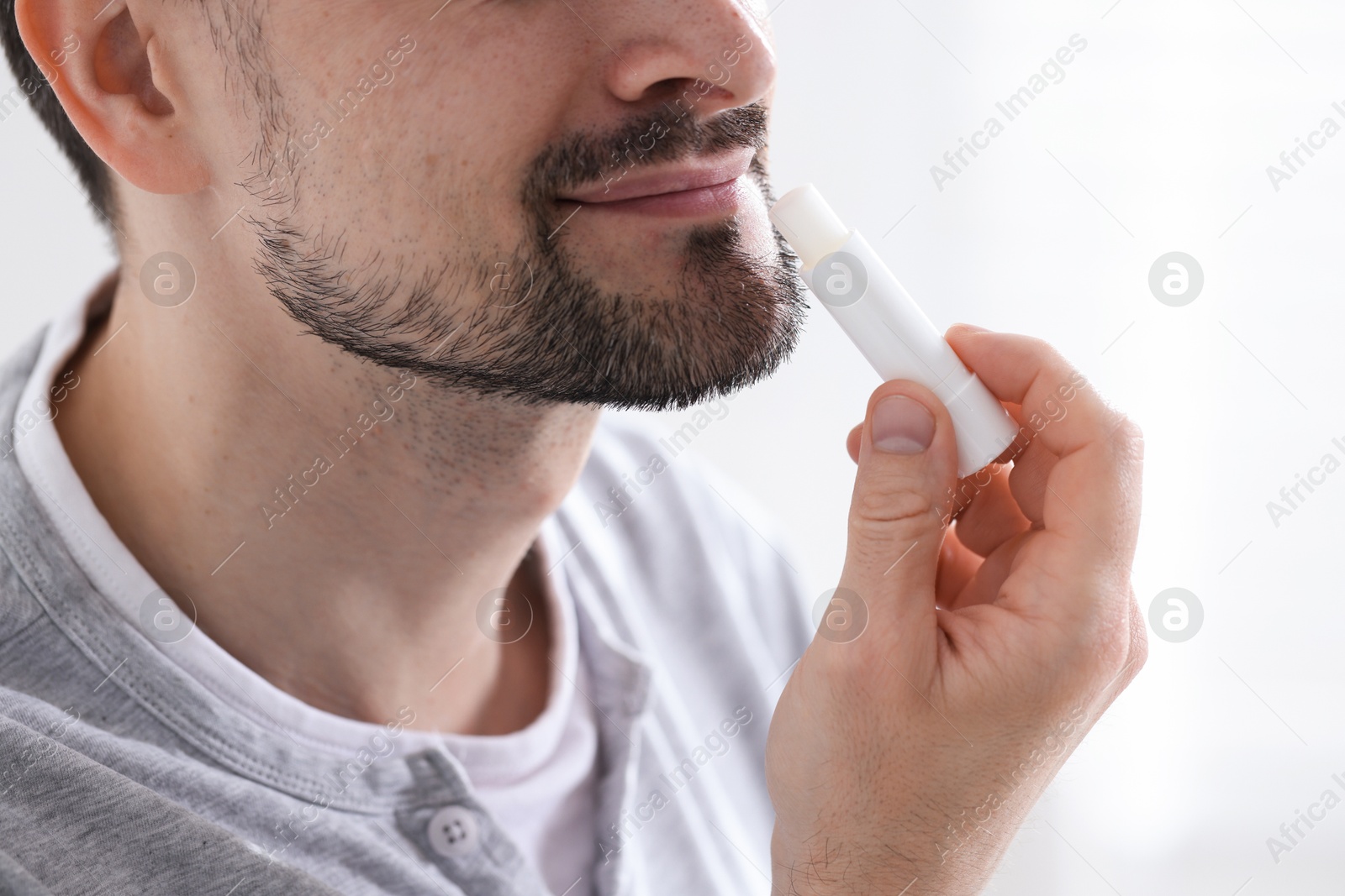 Man applying lip balm onto his lips on blurred light background, closeup Photo of Man applying lip balm onto his lips on blurred light background, closeup