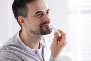 Photo of Handsome man applying lip balm onto his lips on blurred light background