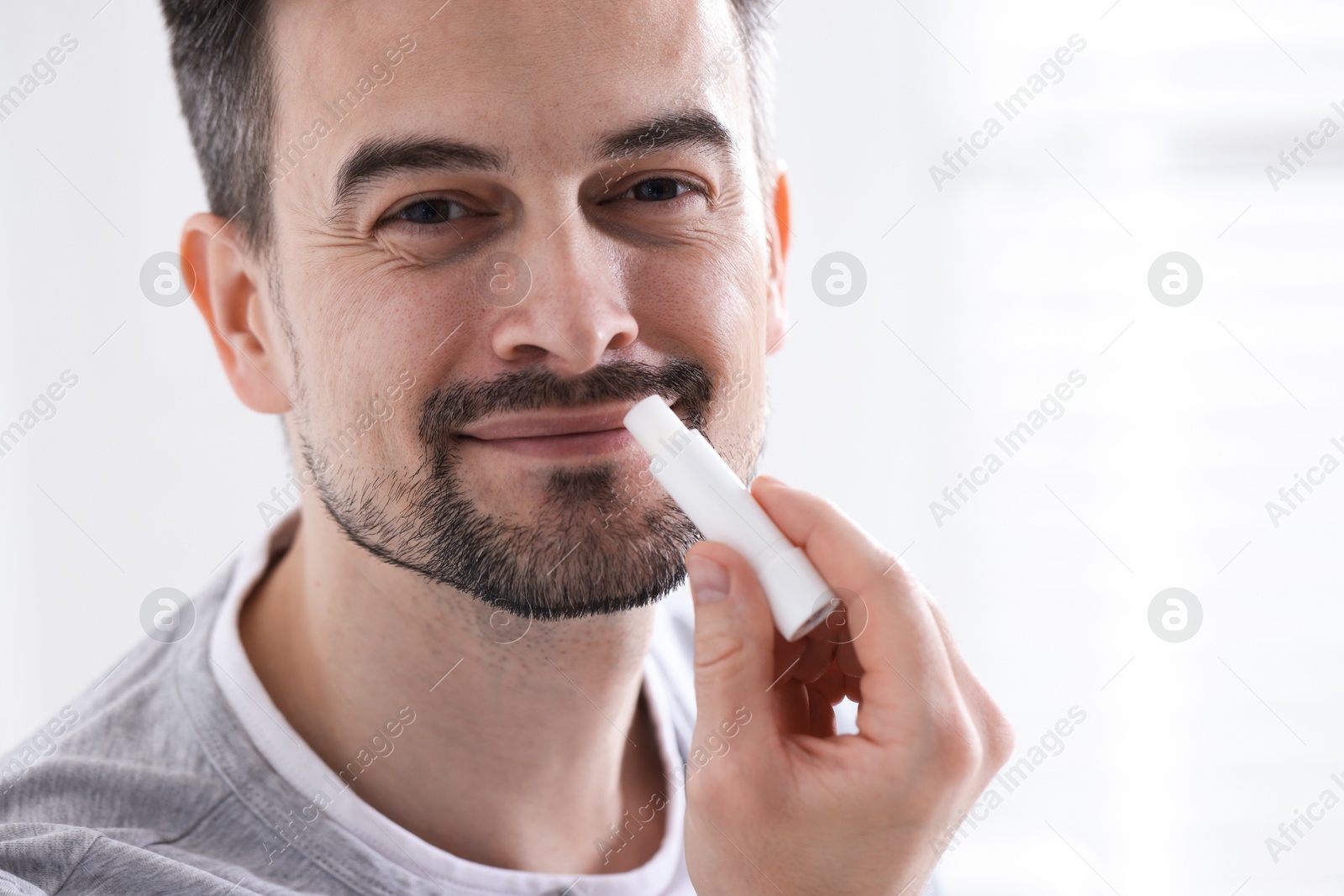 Handsome man applying lip balm onto his lips on blurred light background Photo of Handsome man applying lip balm onto his lips on blurred light background