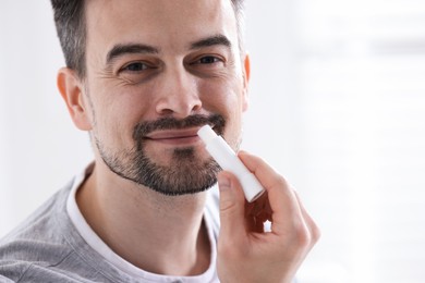Photo of Handsome man applying lip balm onto his lips on blurred light background