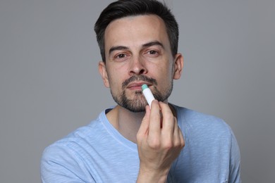 Photo of Handsome man applying lip balm onto his lips on grey background