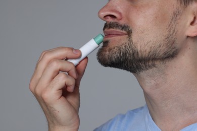 Photo of Man applying lip balm onto his lips on grey background, closeup