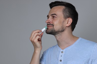 Photo of Handsome man applying lip balm onto his lips on grey background. Space for text