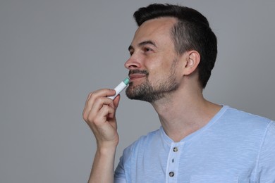 Photo of Handsome man applying lip balm onto his lips on grey background. Space for text