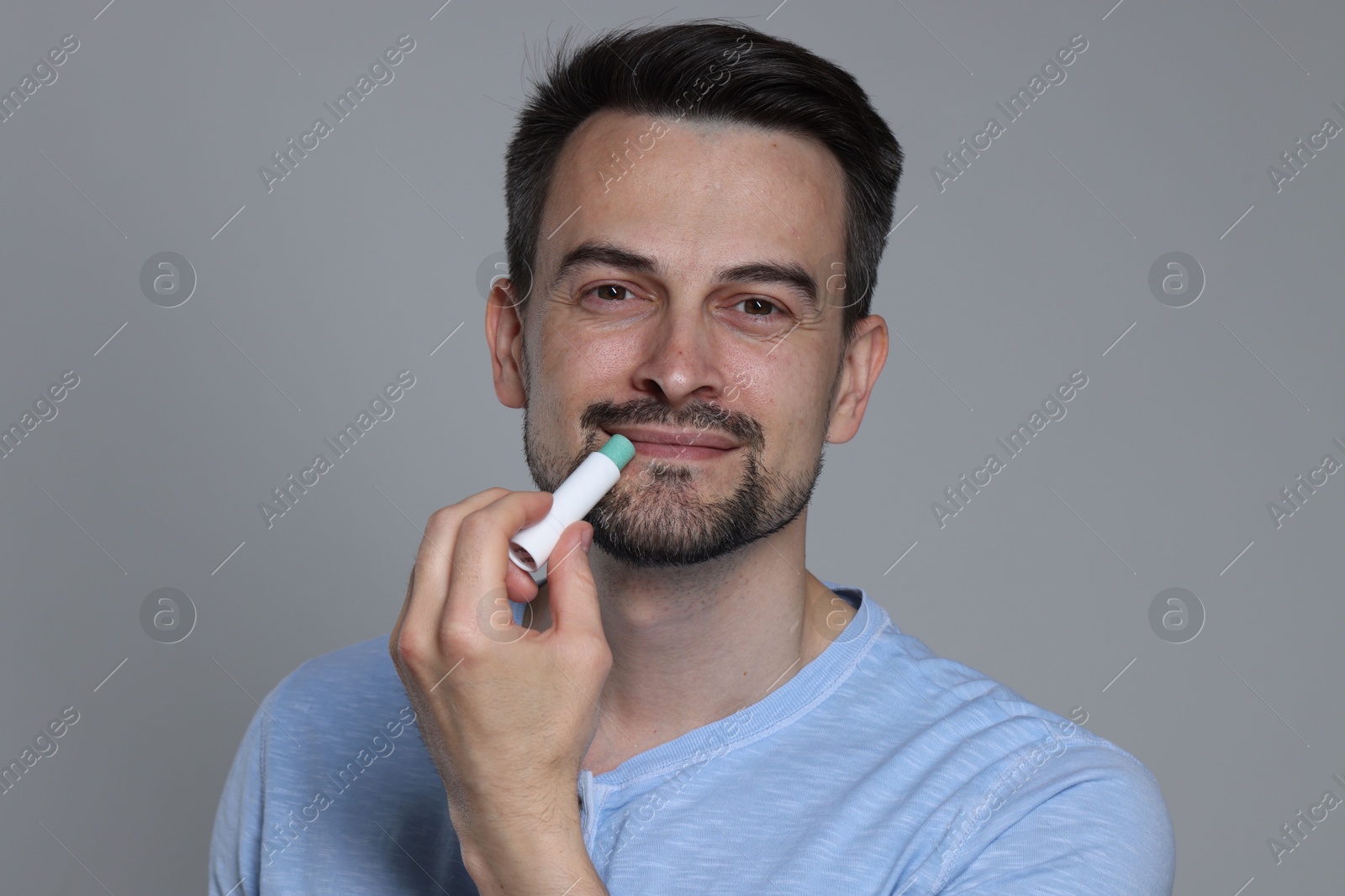 Handsome man applying lip balm onto his lips on grey background Photo of Handsome man applying lip balm onto his lips on grey background