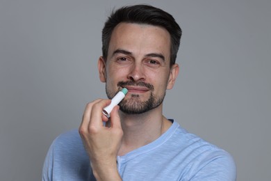 Photo of Handsome man applying lip balm onto his lips on grey background