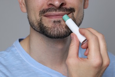 Photo of Man applying lip balm onto his lips on grey background, closeup