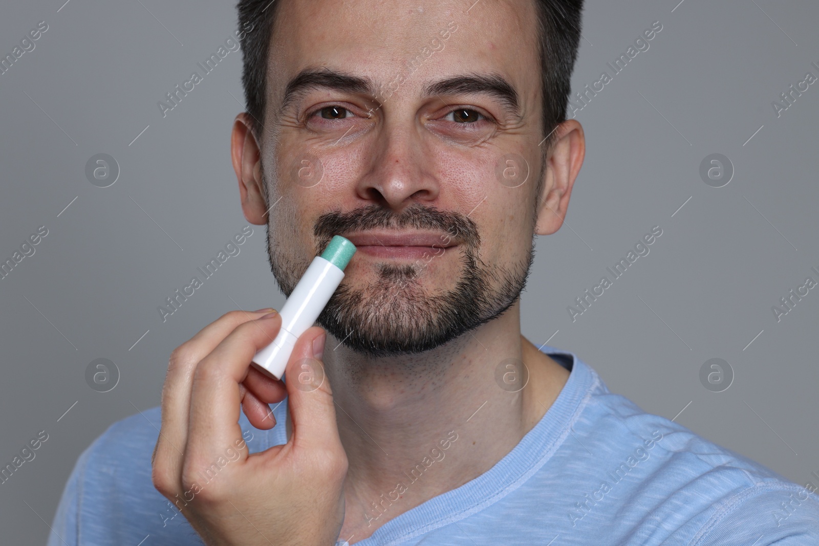 Handsome man applying lip balm onto his lips on grey background Photo of Handsome man applying lip balm onto his lips on grey background