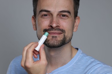 Photo of Handsome man applying lip balm onto his lips on grey background