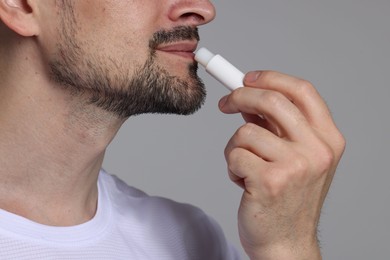 Photo of Man applying lip balm onto his lips on grey background, closeup