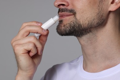 Photo of Man applying lip balm onto his lips on grey background, closeup