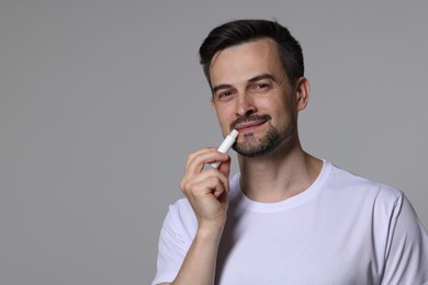 Photo of Handsome man applying lip balm onto his lips on grey background. Space for text
