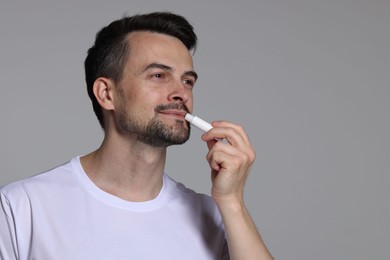 Photo of Handsome man applying lip balm onto his lips on grey background. Space for text