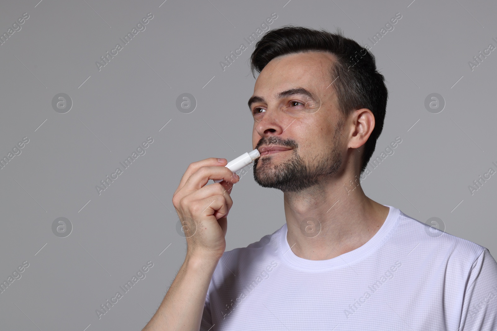 Handsome man applying lip balm onto his lips on grey background. Space for text Photo of Handsome man applying lip balm onto his lips on grey background. Space for text