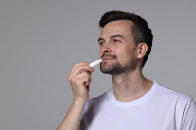 Photo of Handsome man applying lip balm onto his lips on grey background. Space for text