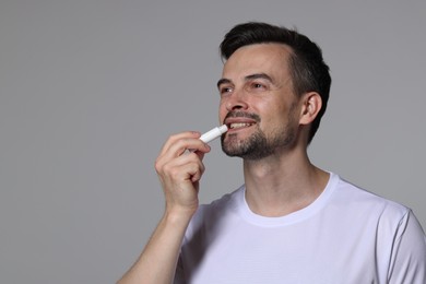Photo of Smiling man applying lip balm onto his lips on grey background. Space for text